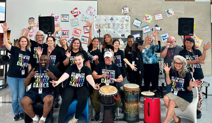 Large group posing with percussion instruments in front of a wall of colorful student artwork.