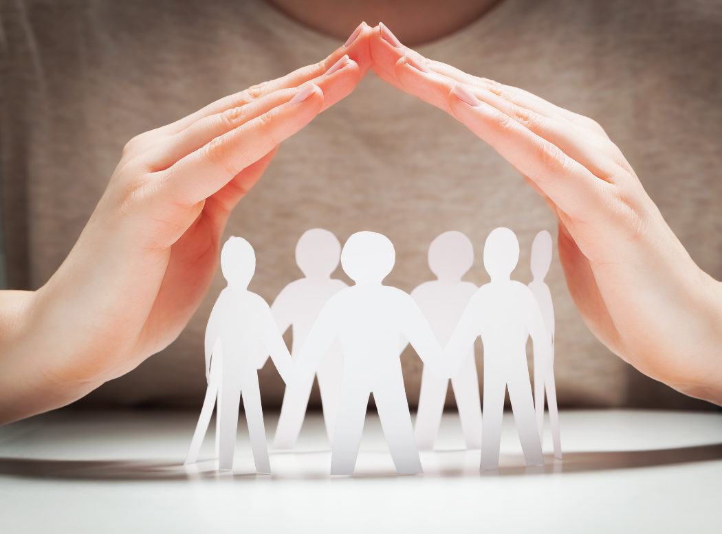 A woman is covering a group of paper people with her hands.