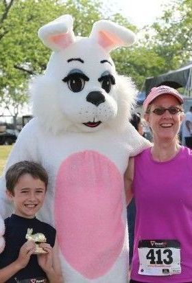 Boy with gold trophy, woman, and bunny mascot pose smiling at a race.