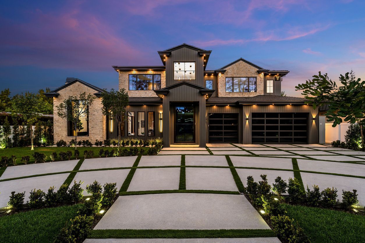 Modern two-story luxury home with stone exterior, lit at dusk, and a landscaped driveway.