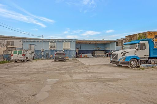A blue and white truck is parked in a dirt lot in front of a building.