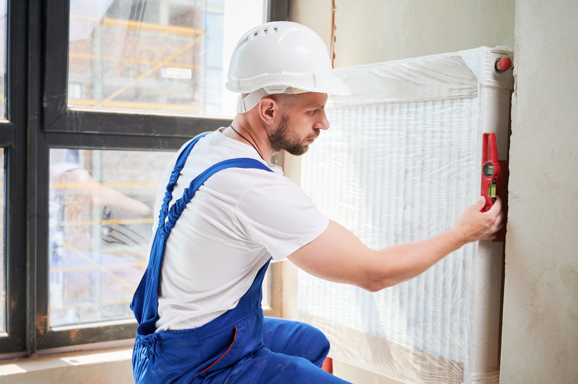 A technician is checking a heating radiator with a spirit level tool at a home
