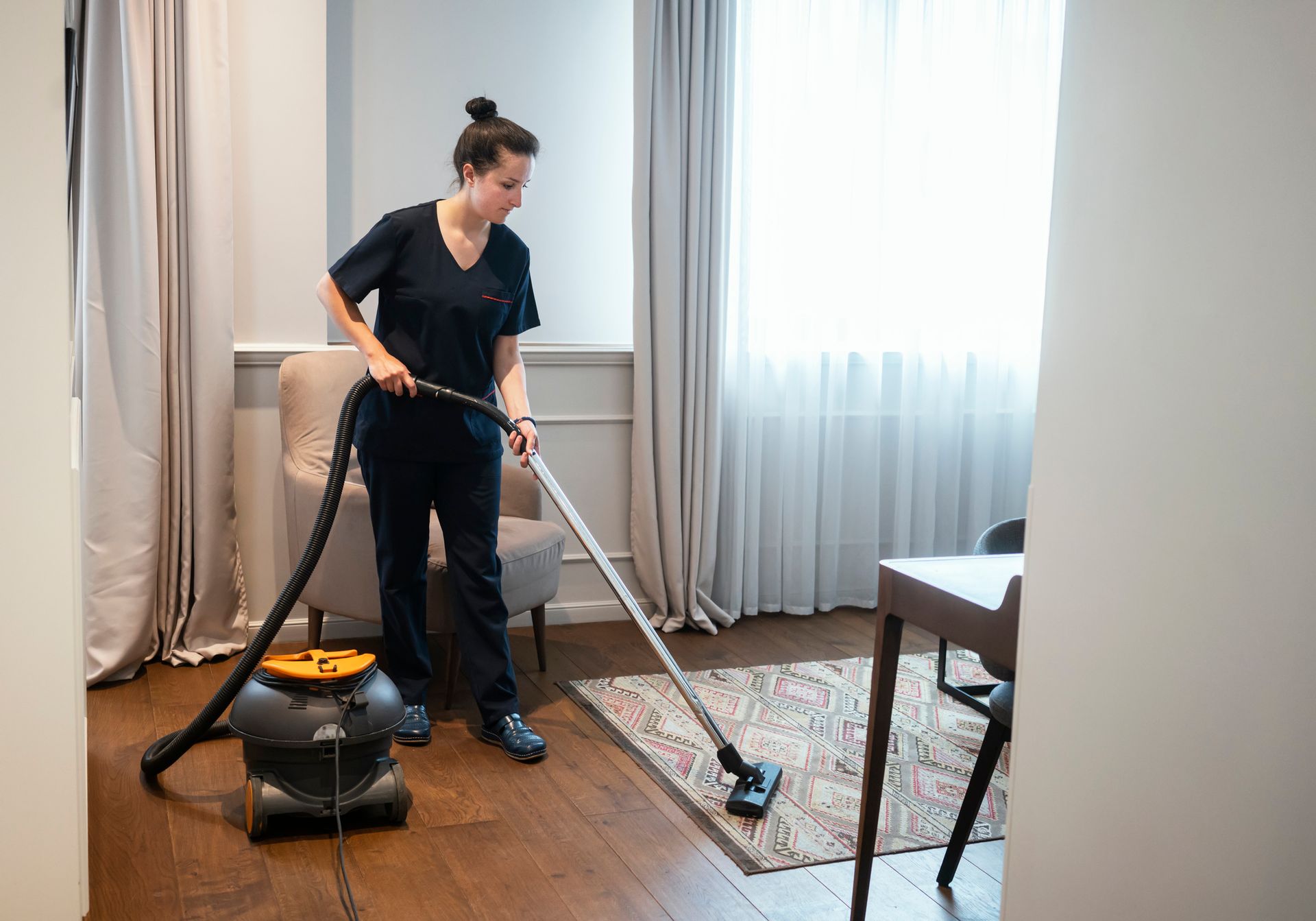 A woman cleaning a room with a vacuum cleaner, emphasizing carpet cleaning and a neat environment.
