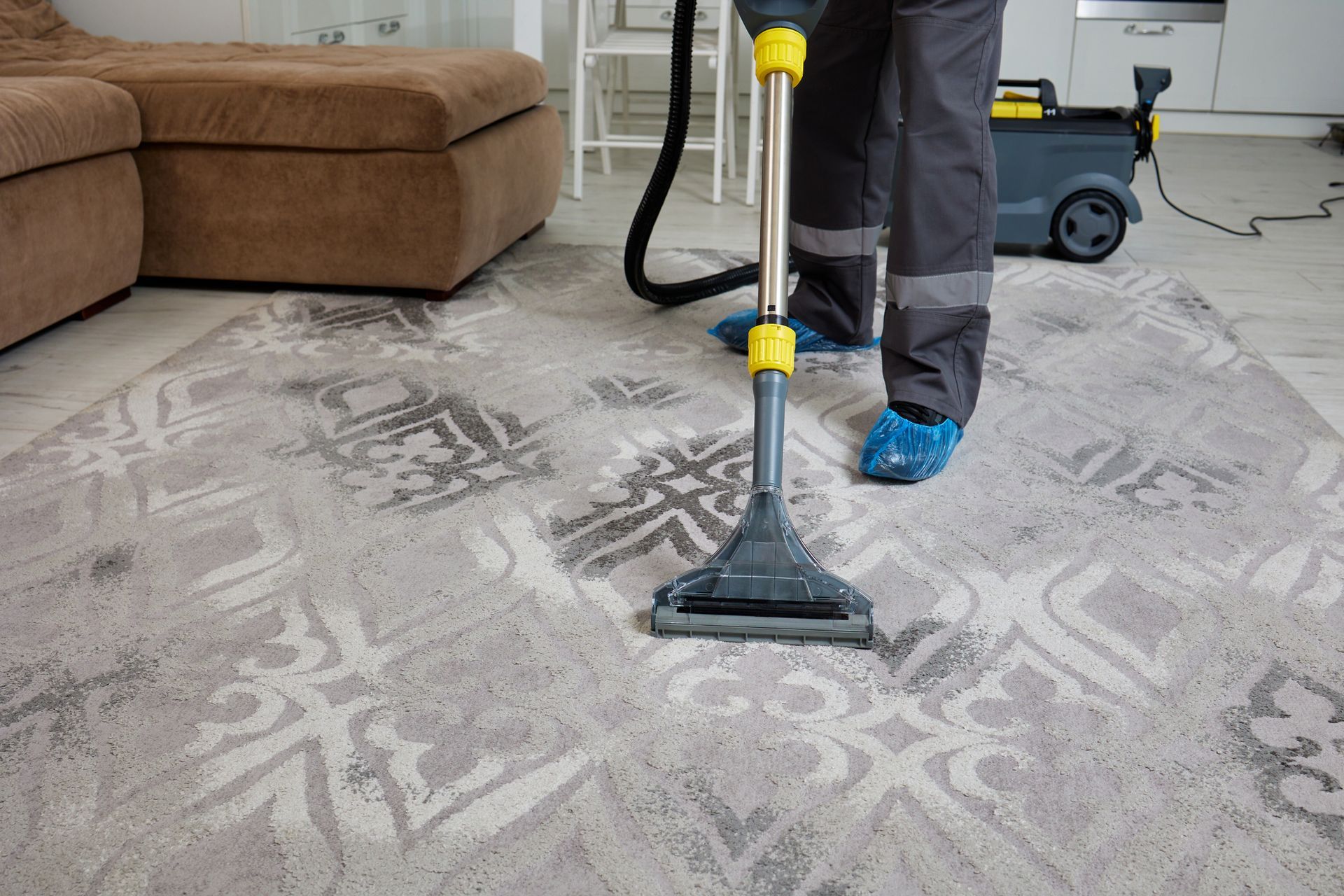 View of a grey carpet being cleaned by a professional carpet cleaning worker with a vacuum.
