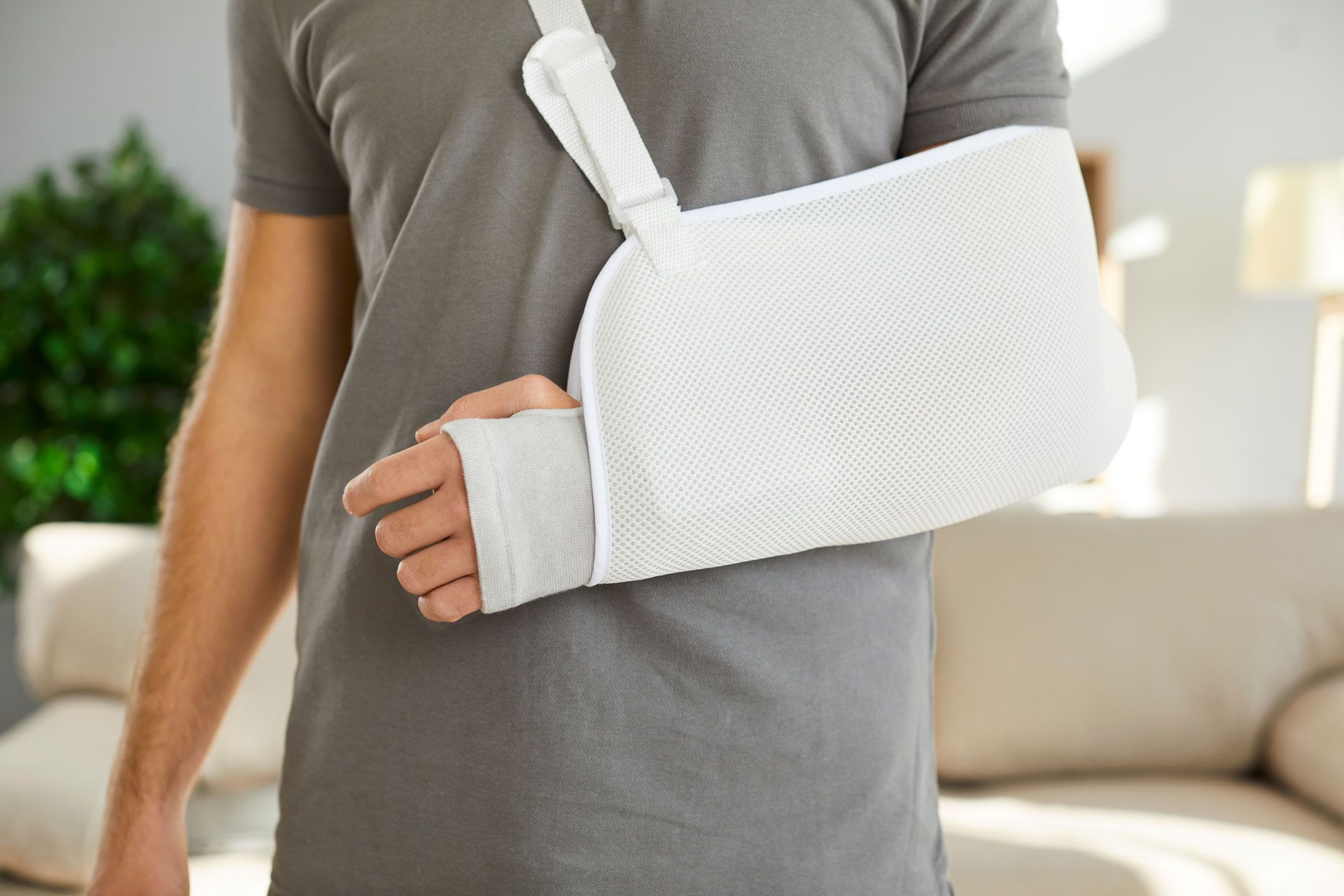 Person wearing a white arm sling on a gray shirt in a living room