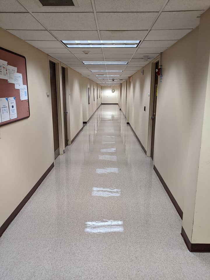 Long, empty office hallway, beige walls, speckled floor, doors on either side, recessed lighting.