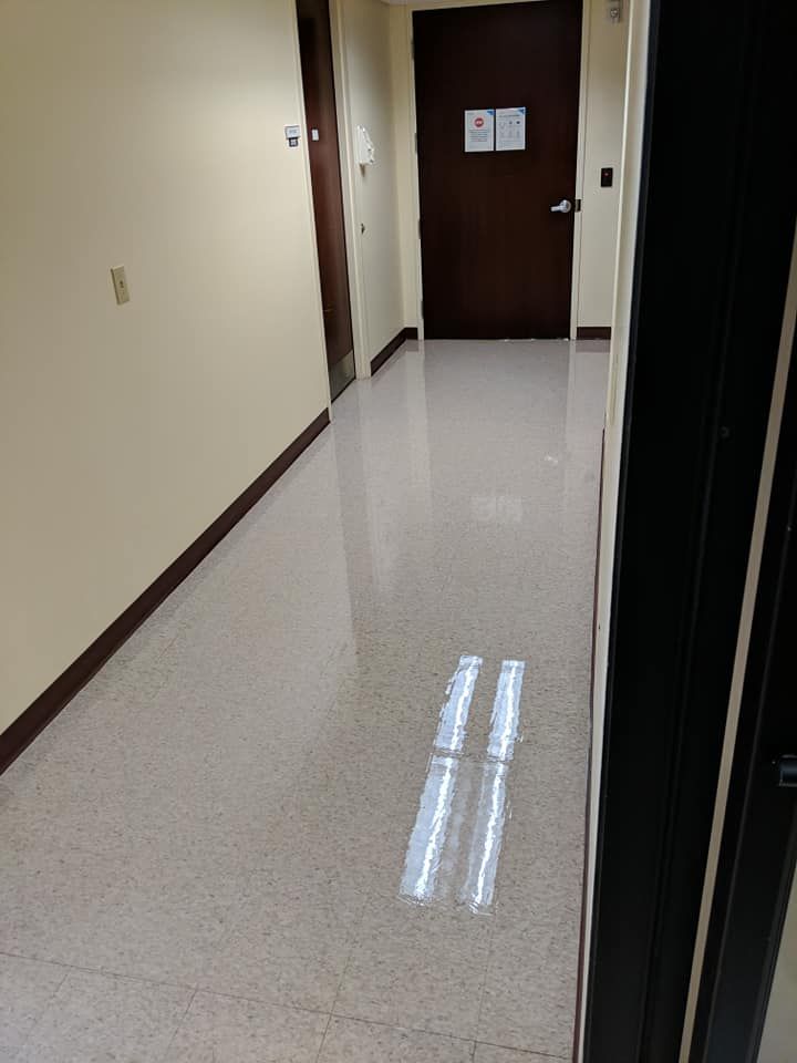 Narrow hallway with beige walls, speckled floor, brown doors, and a light reflection on the floor.