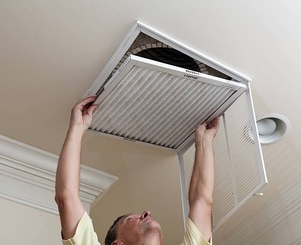 Man replacing air filter in ceiling vent.