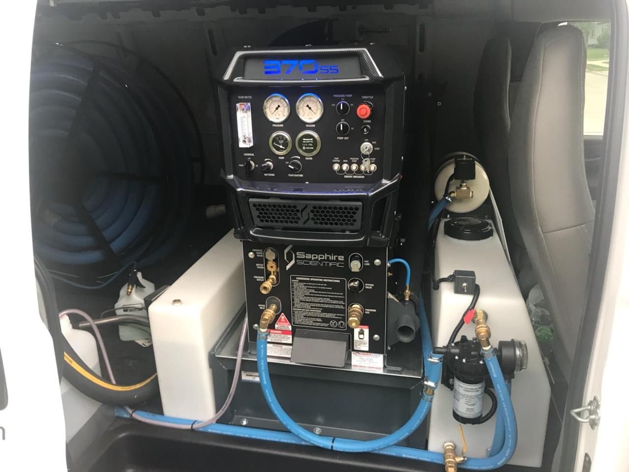Interior of a van with carpet cleaning equipment, including hoses, tanks, and control panel.