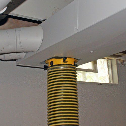 Yellow and black accordion-style hose supports a gray duct in a basement with a window.
