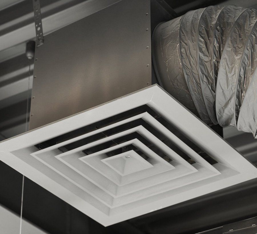 White square air vent in a drop ceiling, connected to a silver duct.