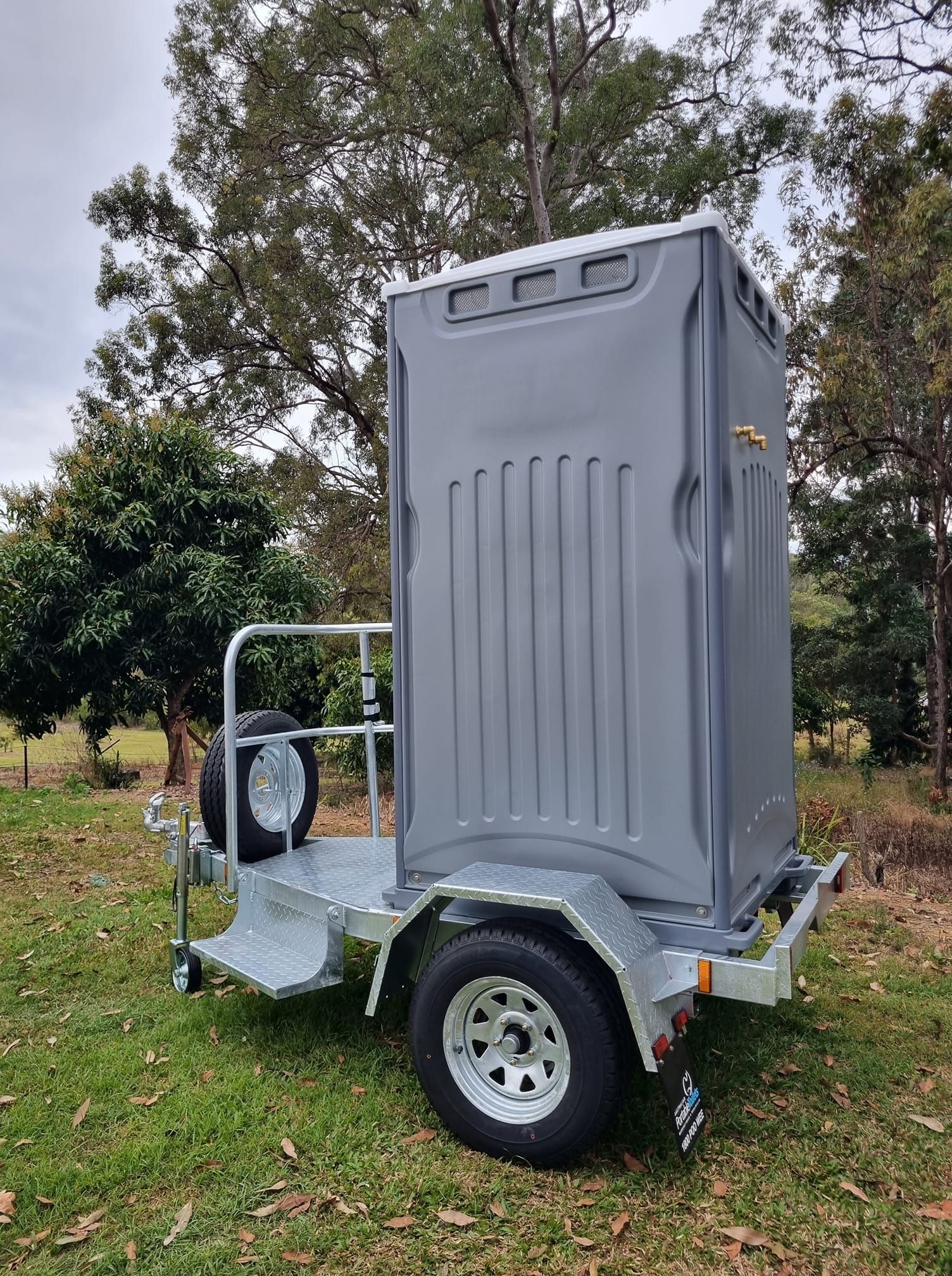 Gray Portable Toilet on a Trailer in a Grassy — Royal Flush Luxury Toilet, Portaloo & Shower Hire in Maryborough, QLD