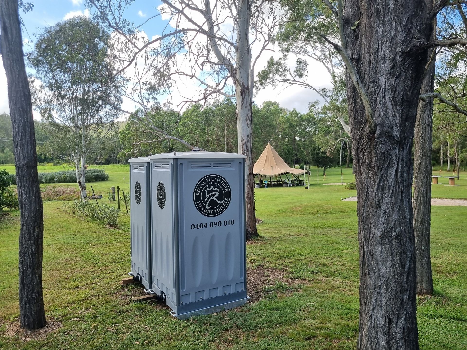 Two Gray Portable Toilets in a Grassy Park — Royal Flush Luxury Toilet, Portaloo & Shower Hire in Hervey Bay, QLD