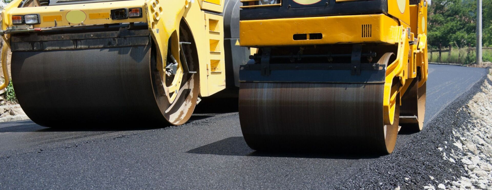 Two yellow asphalt rollers are working on a road.