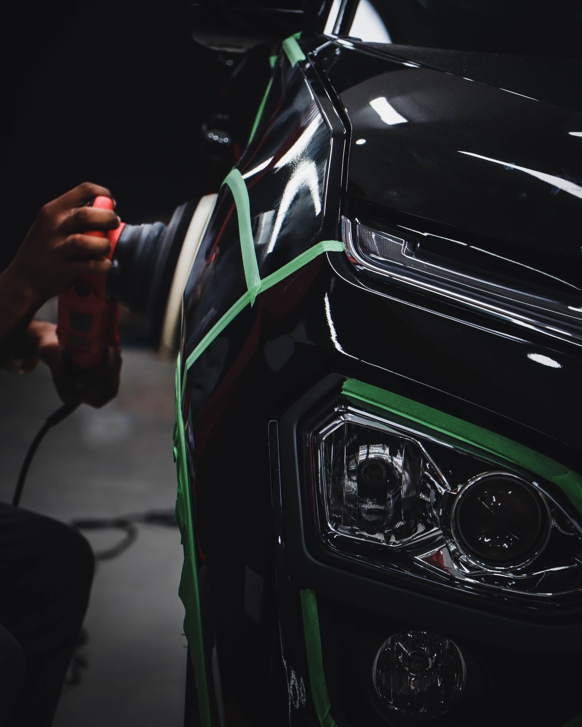 A person is polishing a black car with green tape