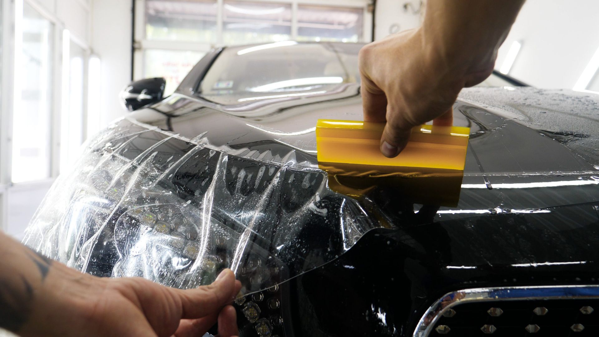 A person is applying protective film to the hood of a car.