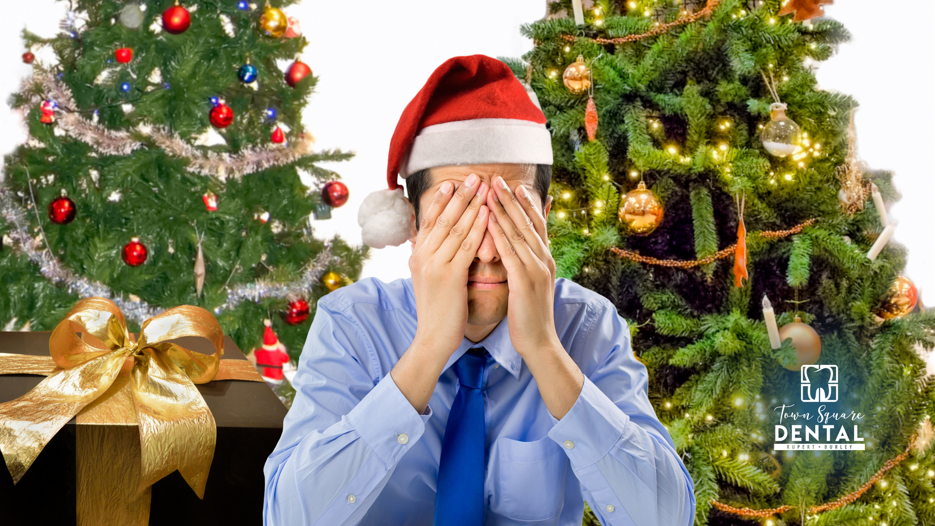 A man in a santa hat is covering his eyes in front of two christmas trees.