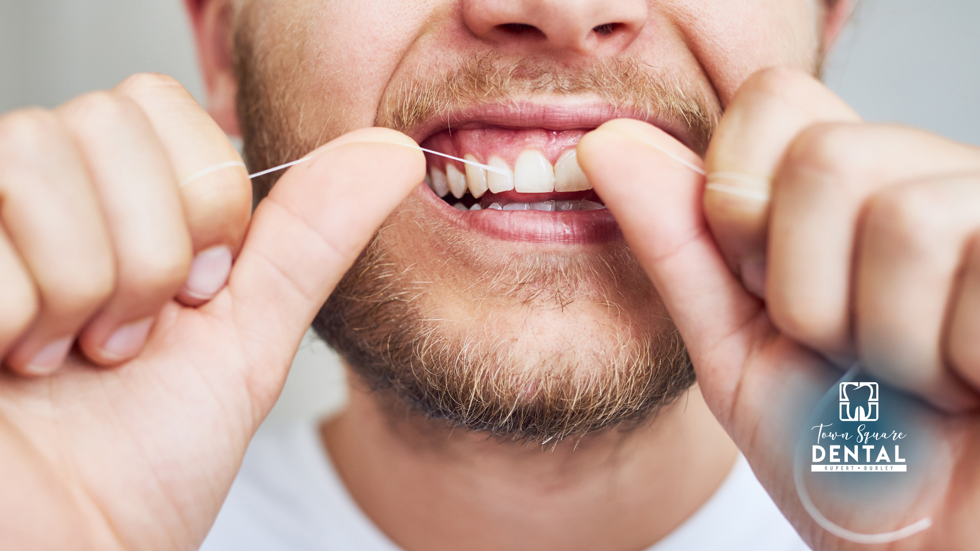 Person flossing teeth, hands holding floss, close-up, teeth visible.