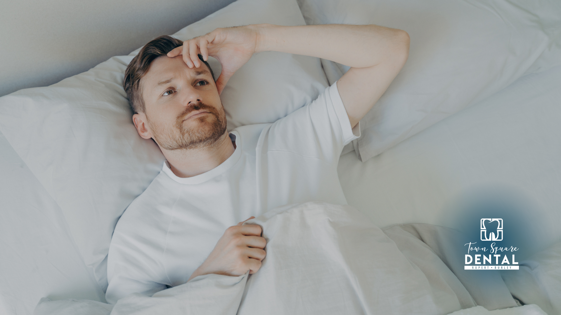 A man is laying in bed with his hand on his forehead.