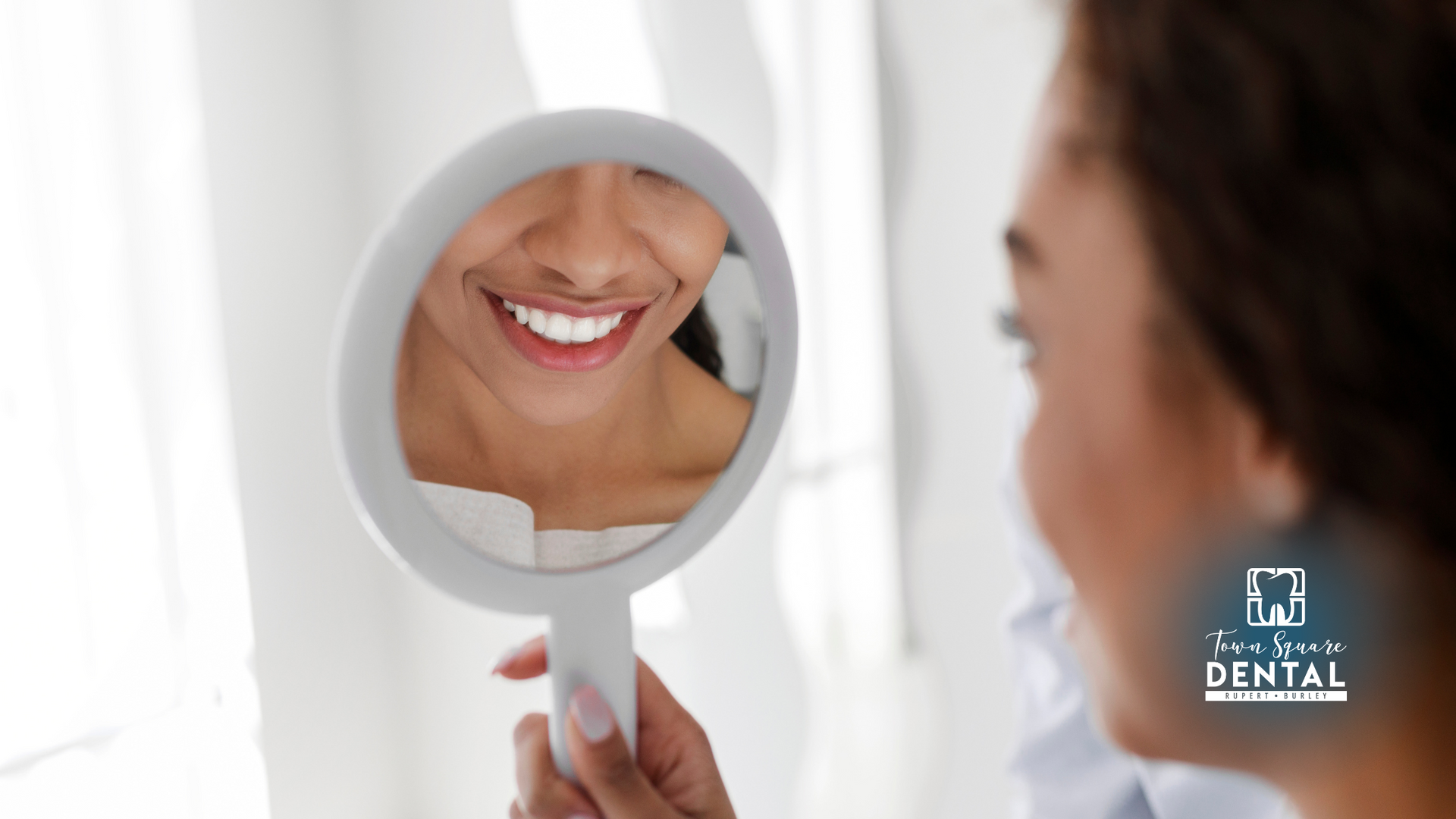 A woman is looking at her smile in a hand mirror.