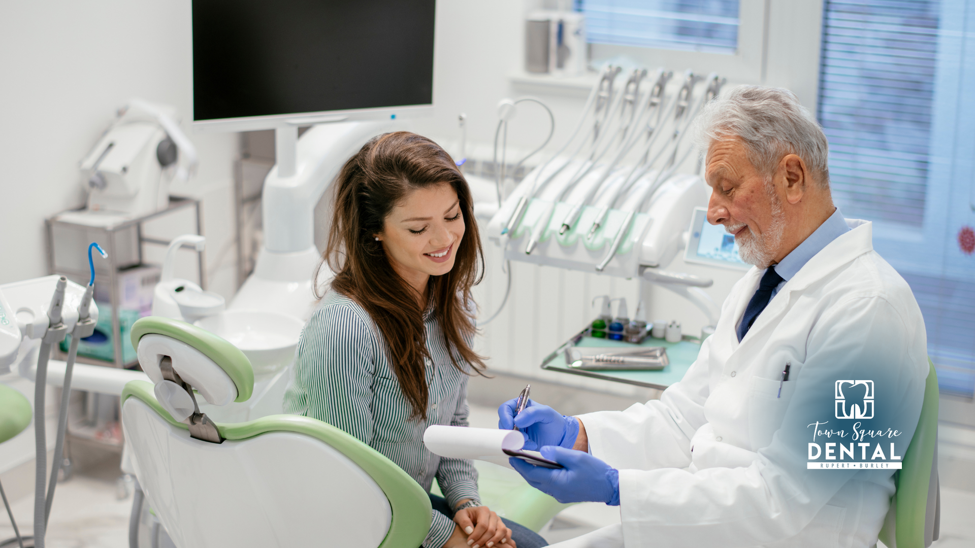 Dentist in white coat consults with a patient in dental chair, looking at a document.