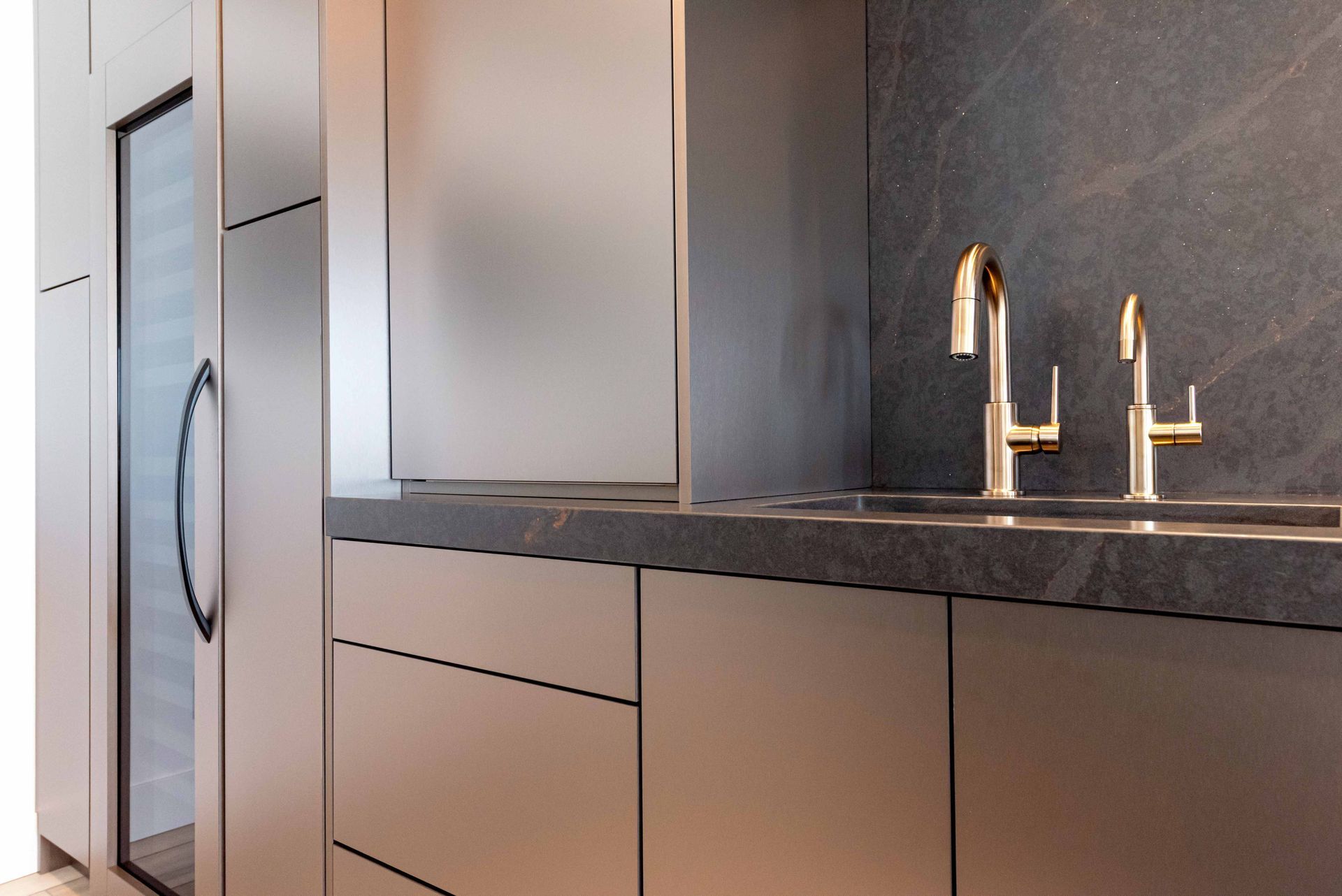 Modern kitchen with metallic cabinets, dark countertop, and gold faucets.