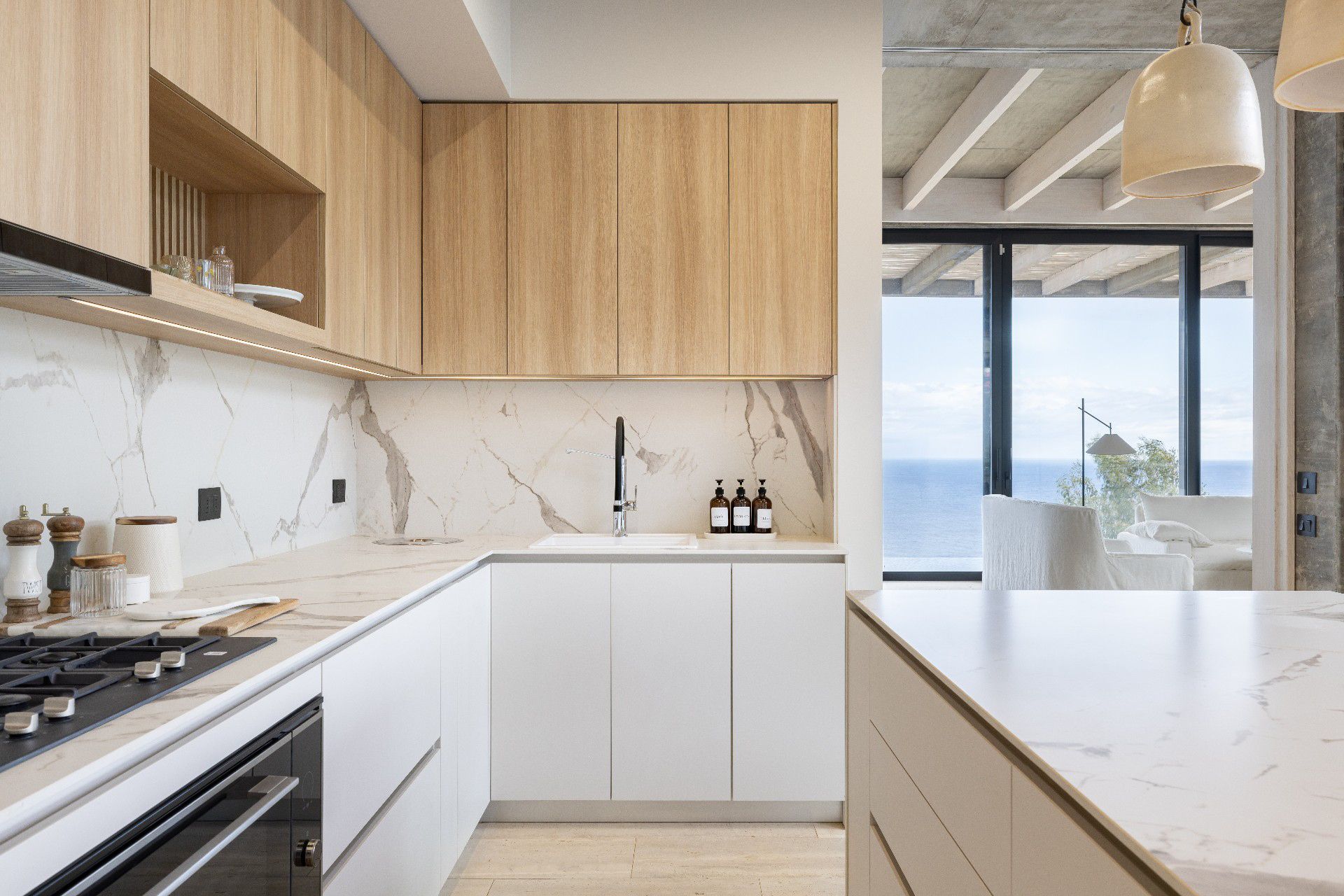 Modern kitchen with wood and white cabinets, marble backsplash and countertops, and ocean view.