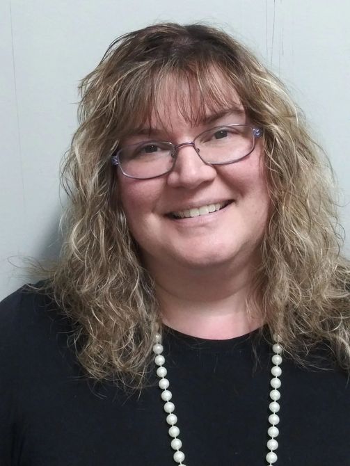 A woman wearing glasses and a pearl necklace is smiling for the camera.