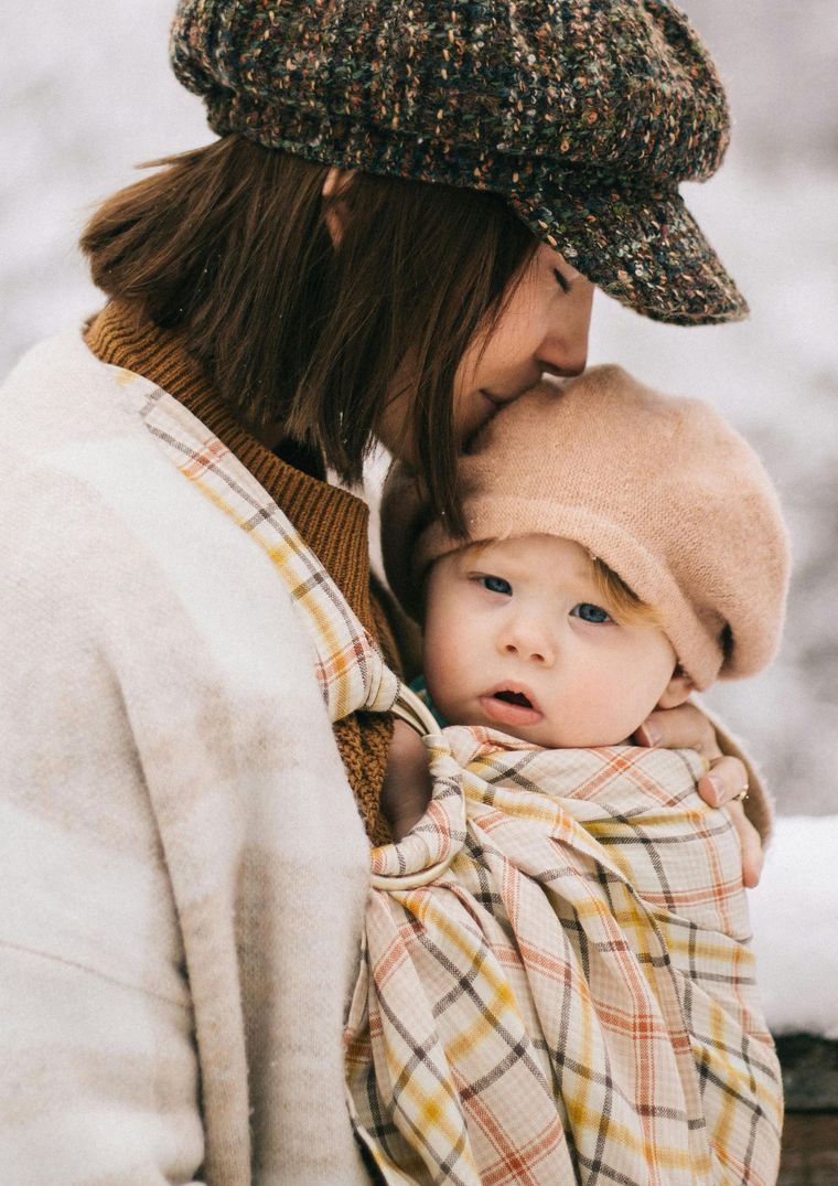 A woman in a hat is holding a baby in a sling.