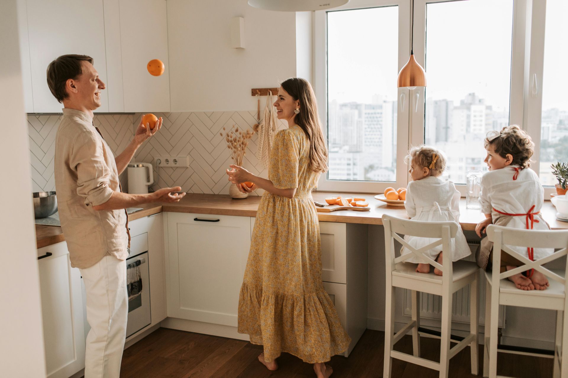 A family is standing in a kitchen playing with oranges.