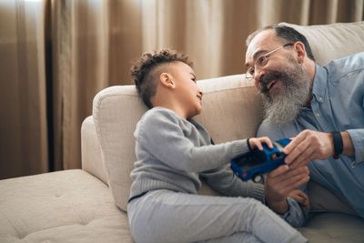 A man and a boy are sitting on a couch playing with a toy car.