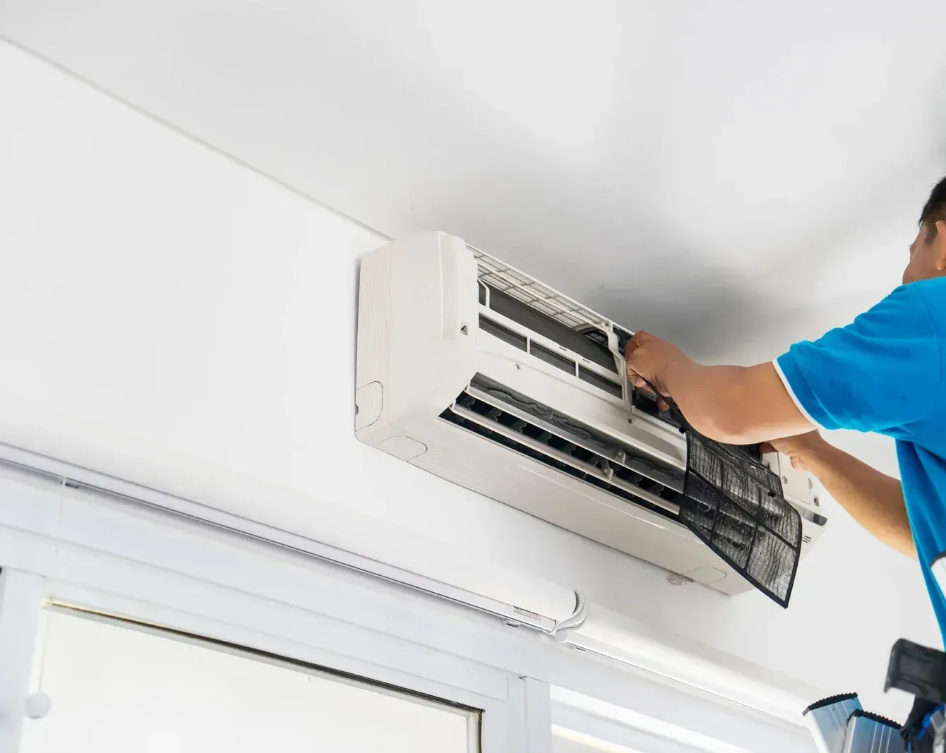 A man is cleaning an air conditioner from the ceiling.