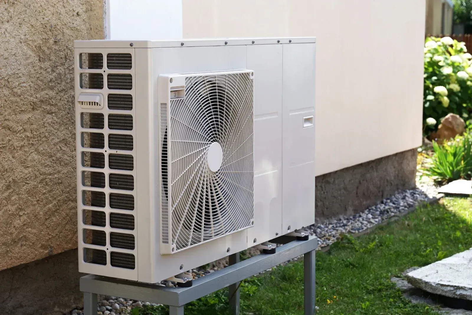 A white air conditioner is sitting on a metal stand outside of a building.