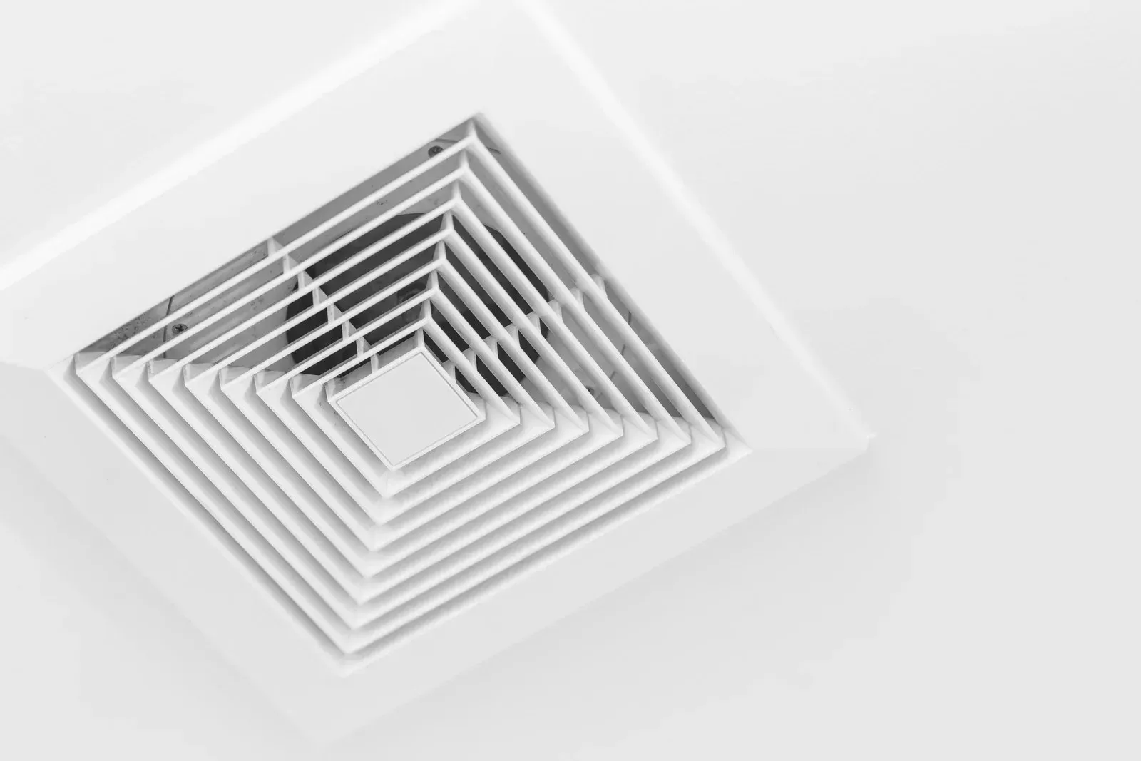 A close up of a white ceiling fan on a white wall.