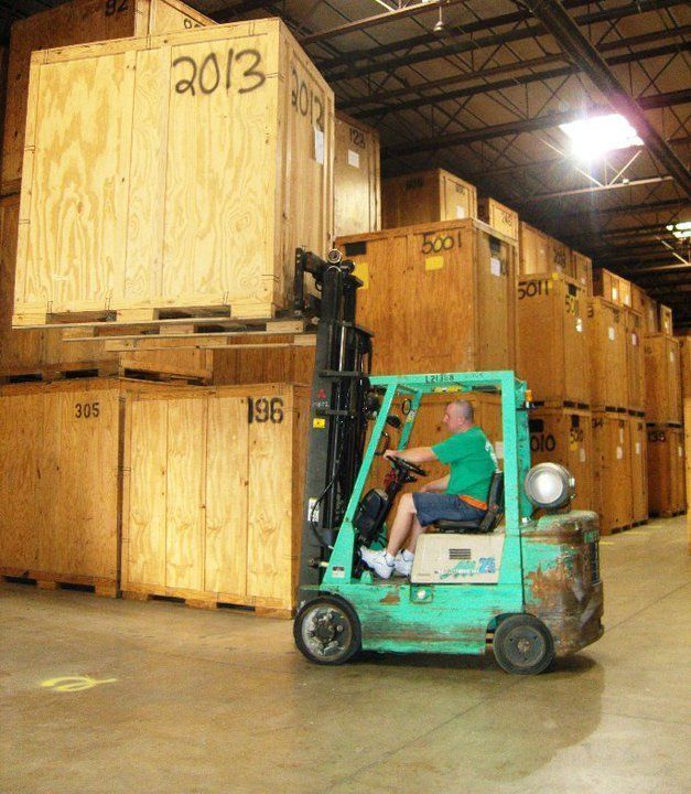 A man is driving a forklift in a warehouse filled with wooden boxes with the year 2013 on them