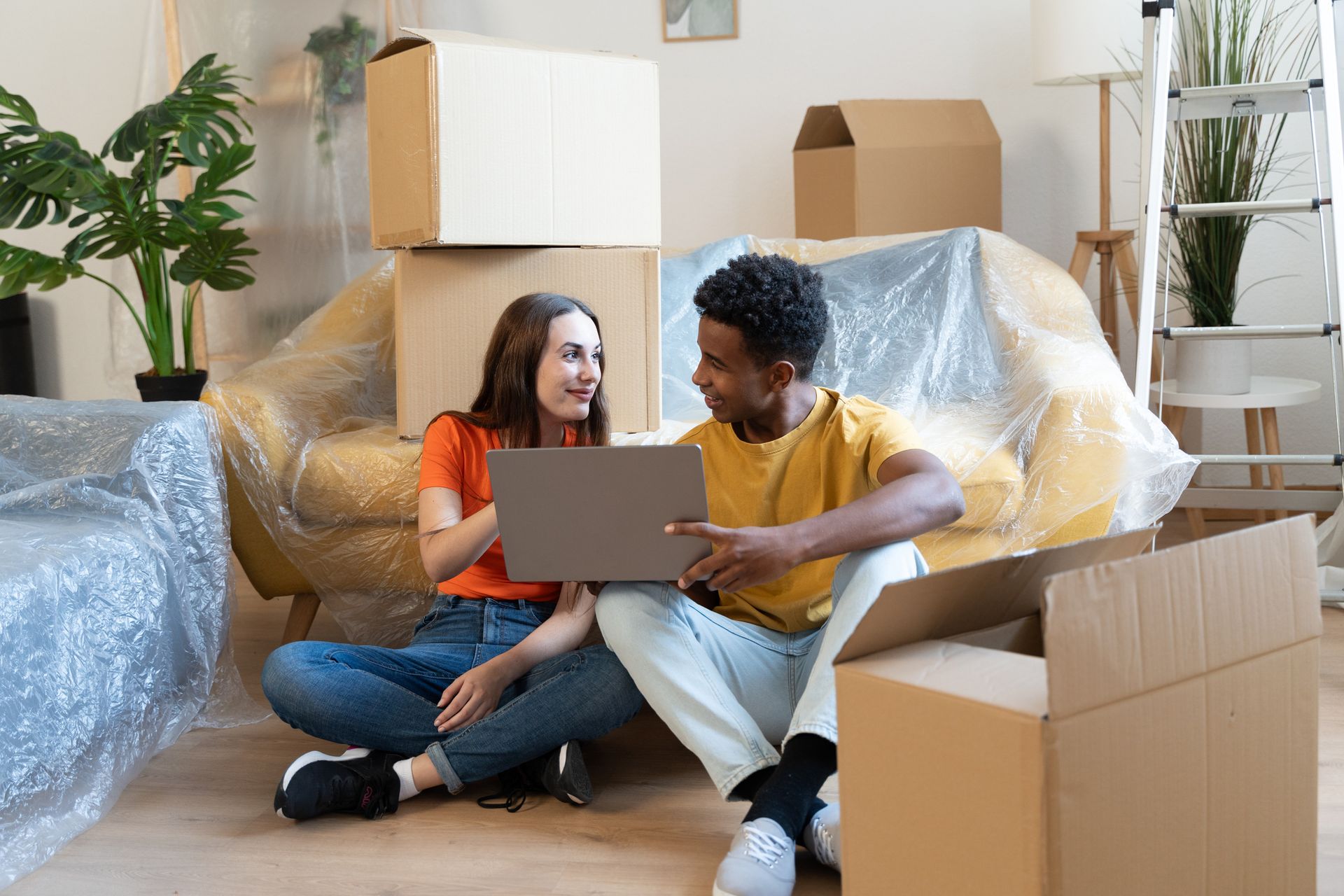 A man and a woman are sitting on the floor in a living room looking at a laptop.