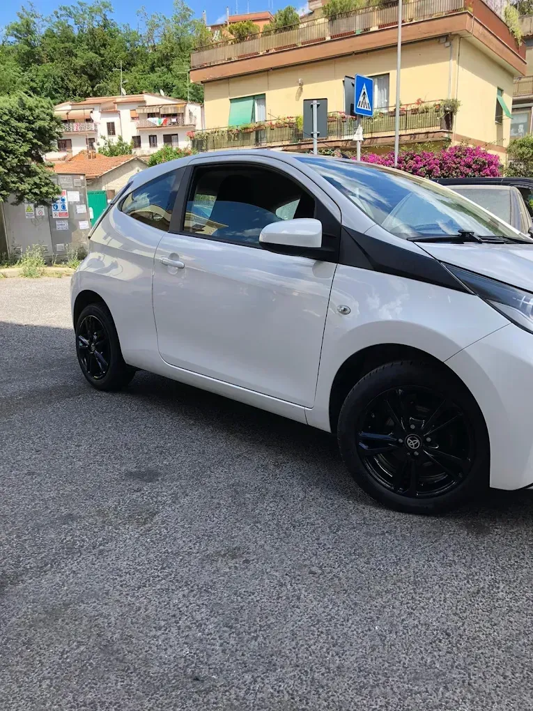Un'auto bianca con ruote nere parcheggiata su una strada di fronte agli edifici.
