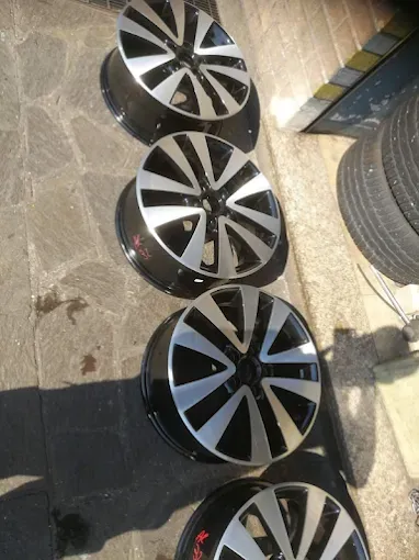 Quattro cerchioni d'auto argentati e neri allineati su una superficie di cemento grigio.