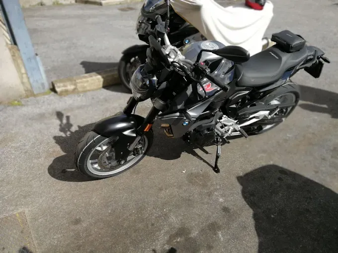 Motocicletta nera e grigia parcheggiata sull'asfalto, in un ambiente soleggiato all'aperto.