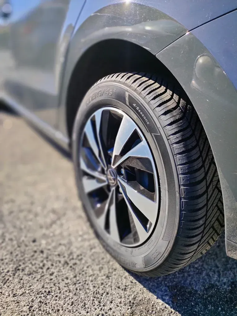 Primo piano di una ruota di automobile con pneumatico nero e cerchione argento e grigio, su una superficie ghiaiosa.