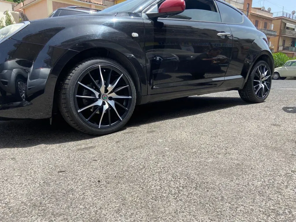 Un'Alfa Romeo MiTo nera con cerchi neri e argento parcheggiata sull'asfalto.