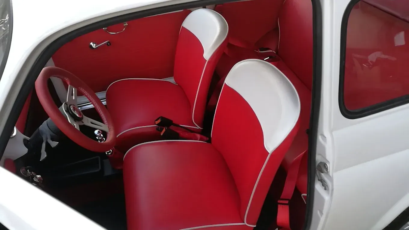 Interni dell'auto rossi e bianchi con sedili avvolgenti, volante e finiture delle portiere; esterno dell'auto bianco visibile.
