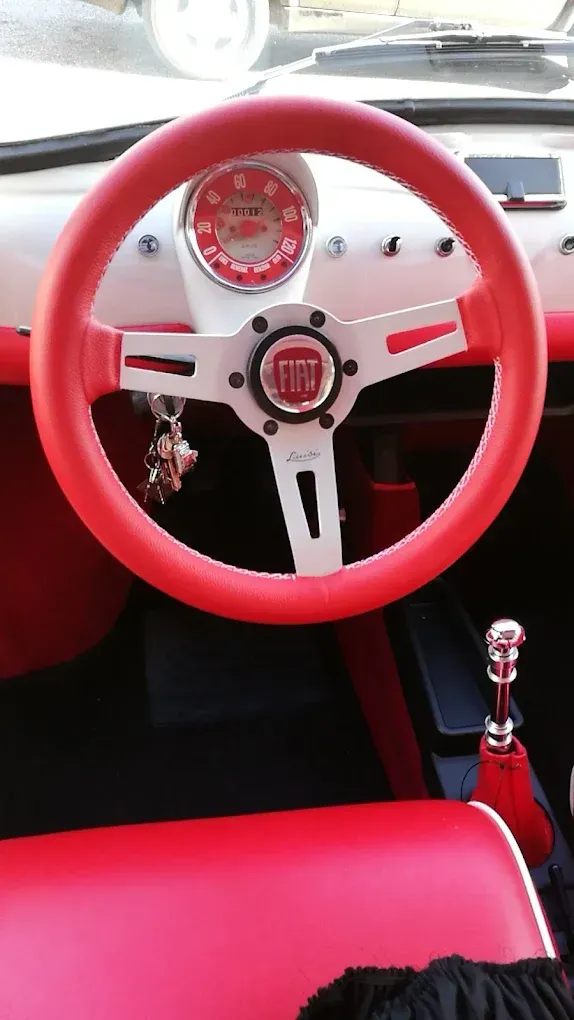 Interni rossi di un'auto Fiat d'epoca con volante e cruscotto rossi.