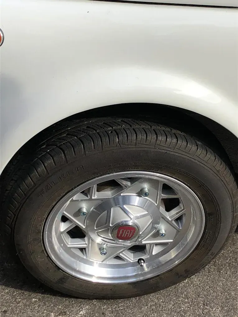 Primo piano della ruota anteriore di un'auto bianca con cerchione argentato a forma di stella e pneumatico nero.