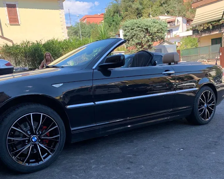 Una BMW nera decappottabile parcheggiata all'esterno con una persona visibile sullo sfondo.