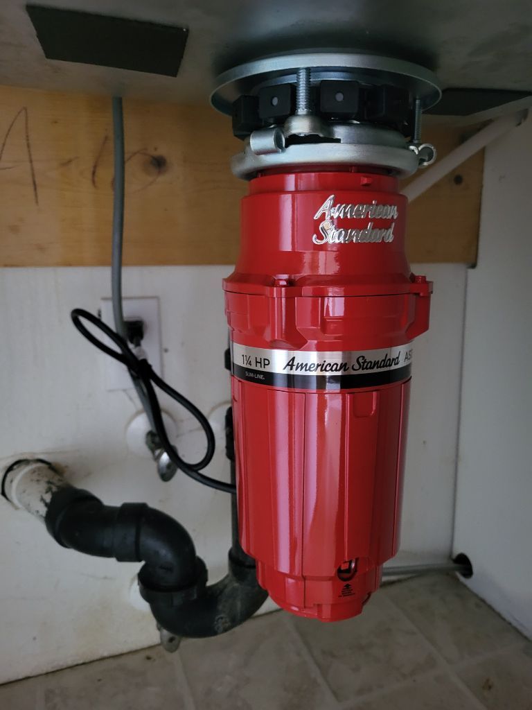 A red garbage disposal is sitting under a sink.
