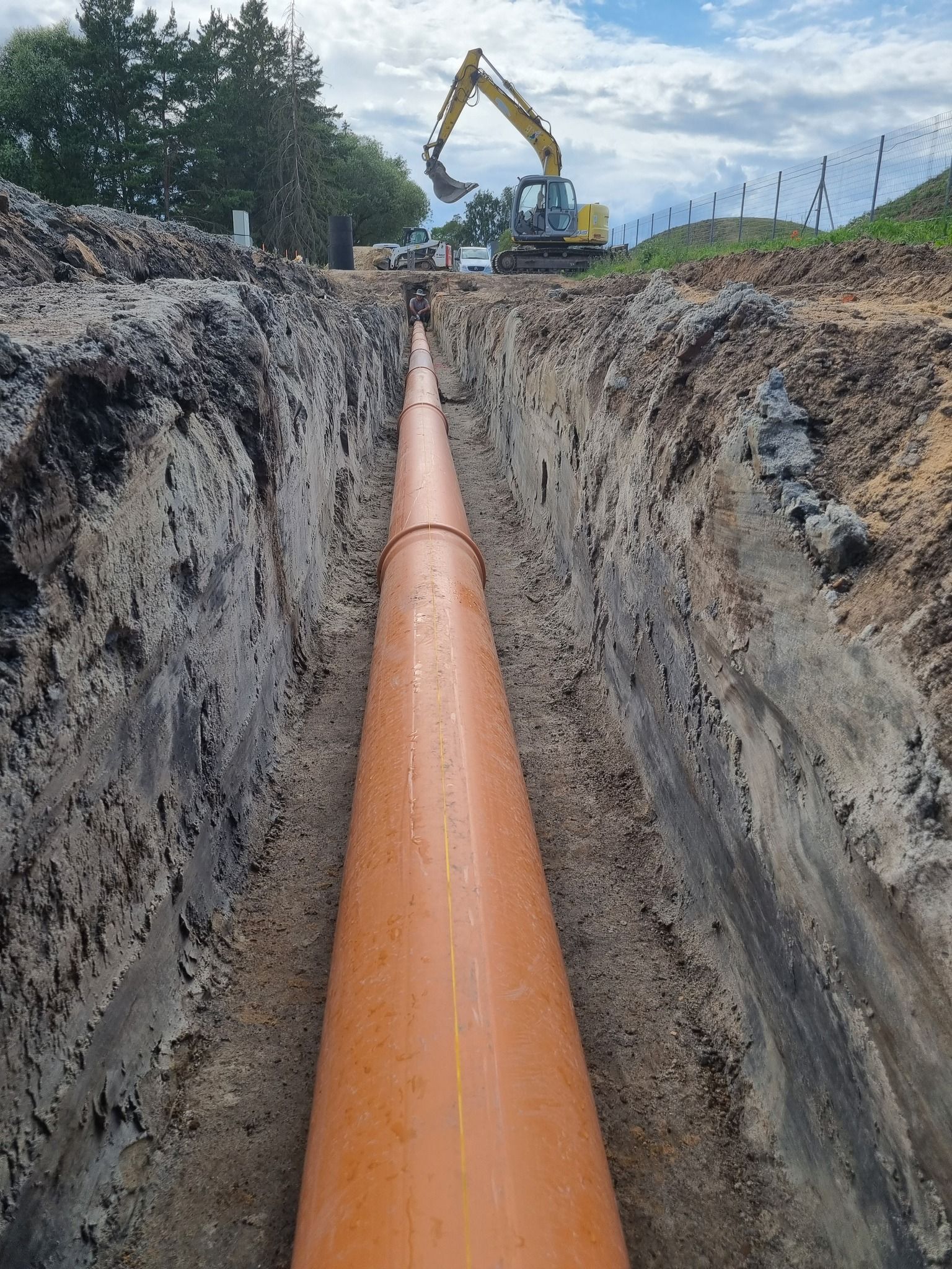 Tranšėjoje montuojamas didelis oranžinis vamzdis.