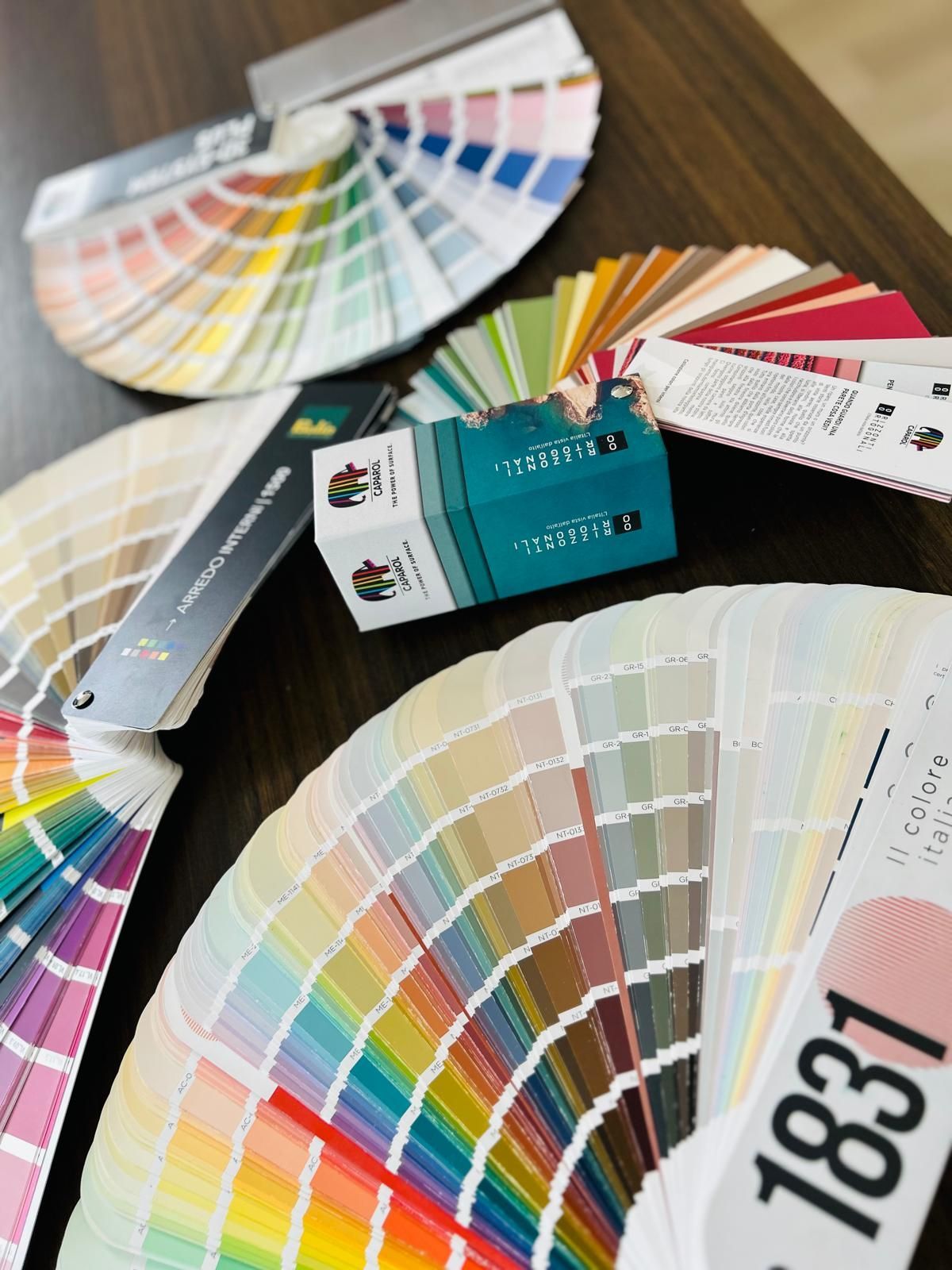 Diversi campionari di colori disposti a ventaglio su una superficie di legno con una piccola scatola blu al centro.