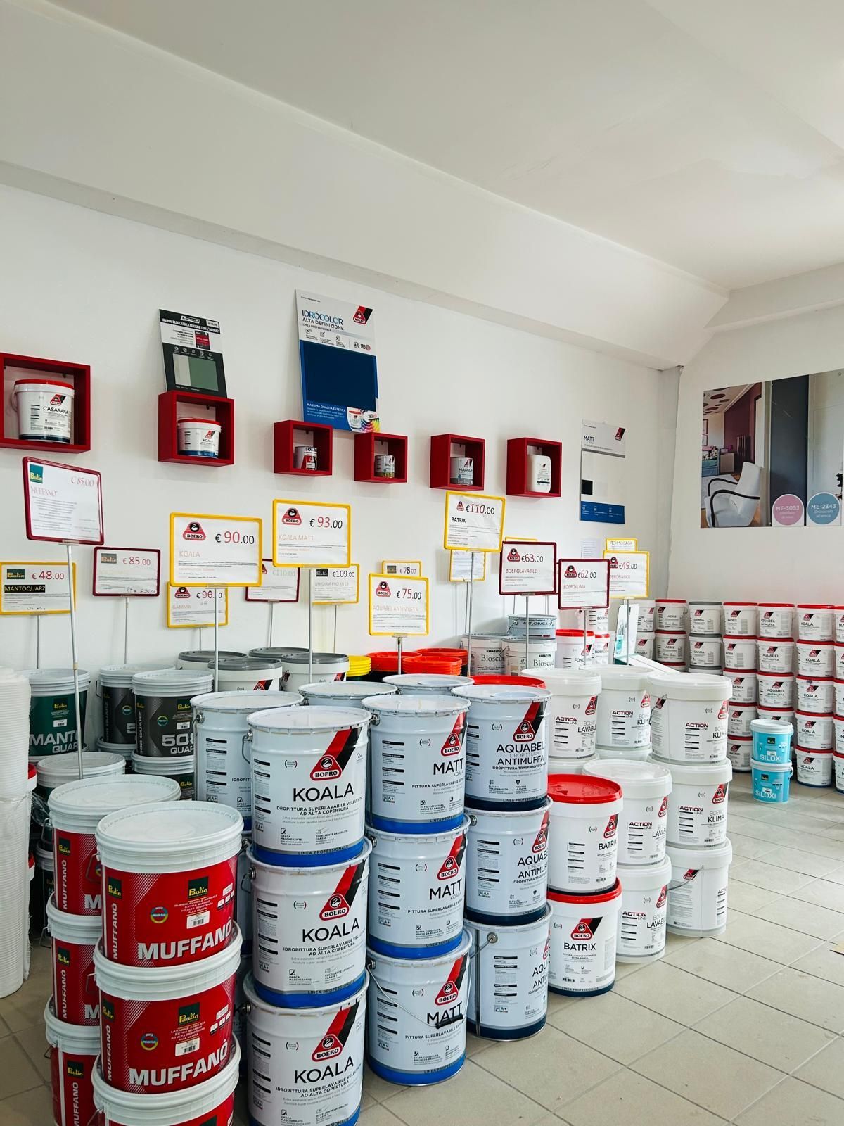 Interno di un negozio al dettaglio con scaffali pieni di secchi di vernice impilati in file contro una parete con cartellini dei prodotti.
