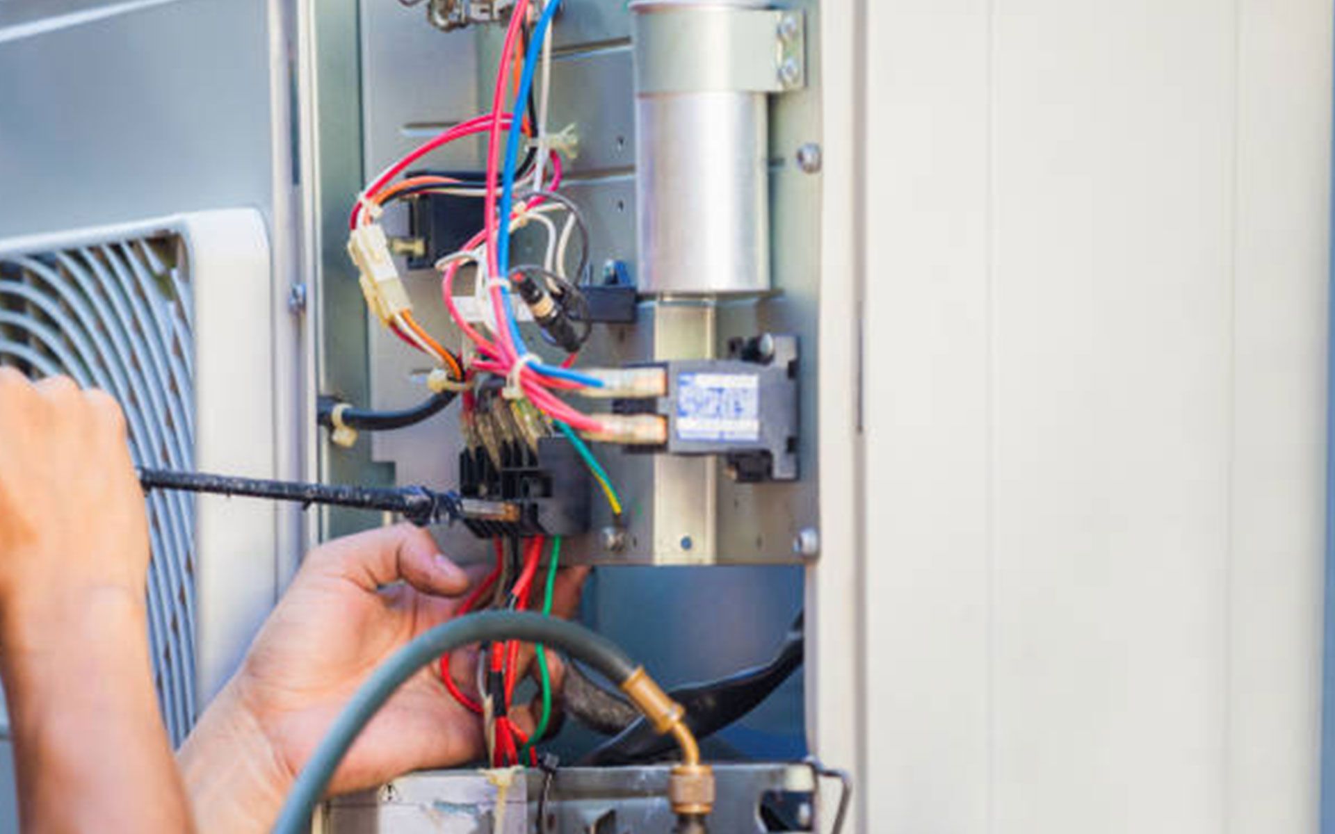 A man is working on an air conditioner with a screwdriver.
